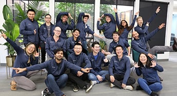 A group of people wearing matching black jackets with Orby AI logo as they pose for a picture in the office